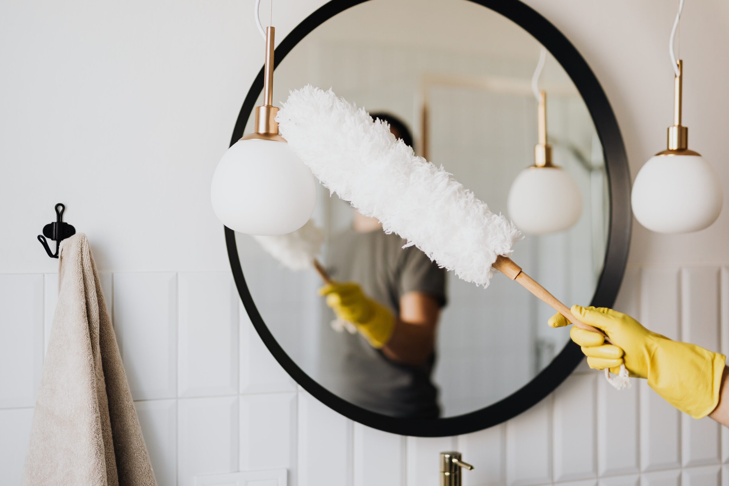 Person cleaning bathroom mirror and lamps with a duster