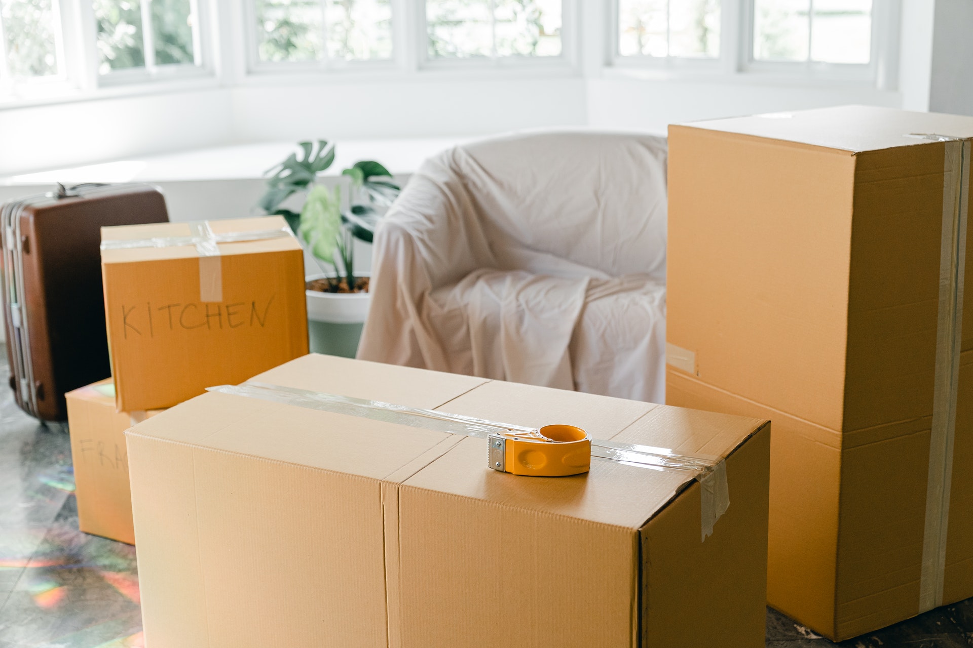 Boxes labelled "Kitchen" next to a suitcase and a couch covered in cloth