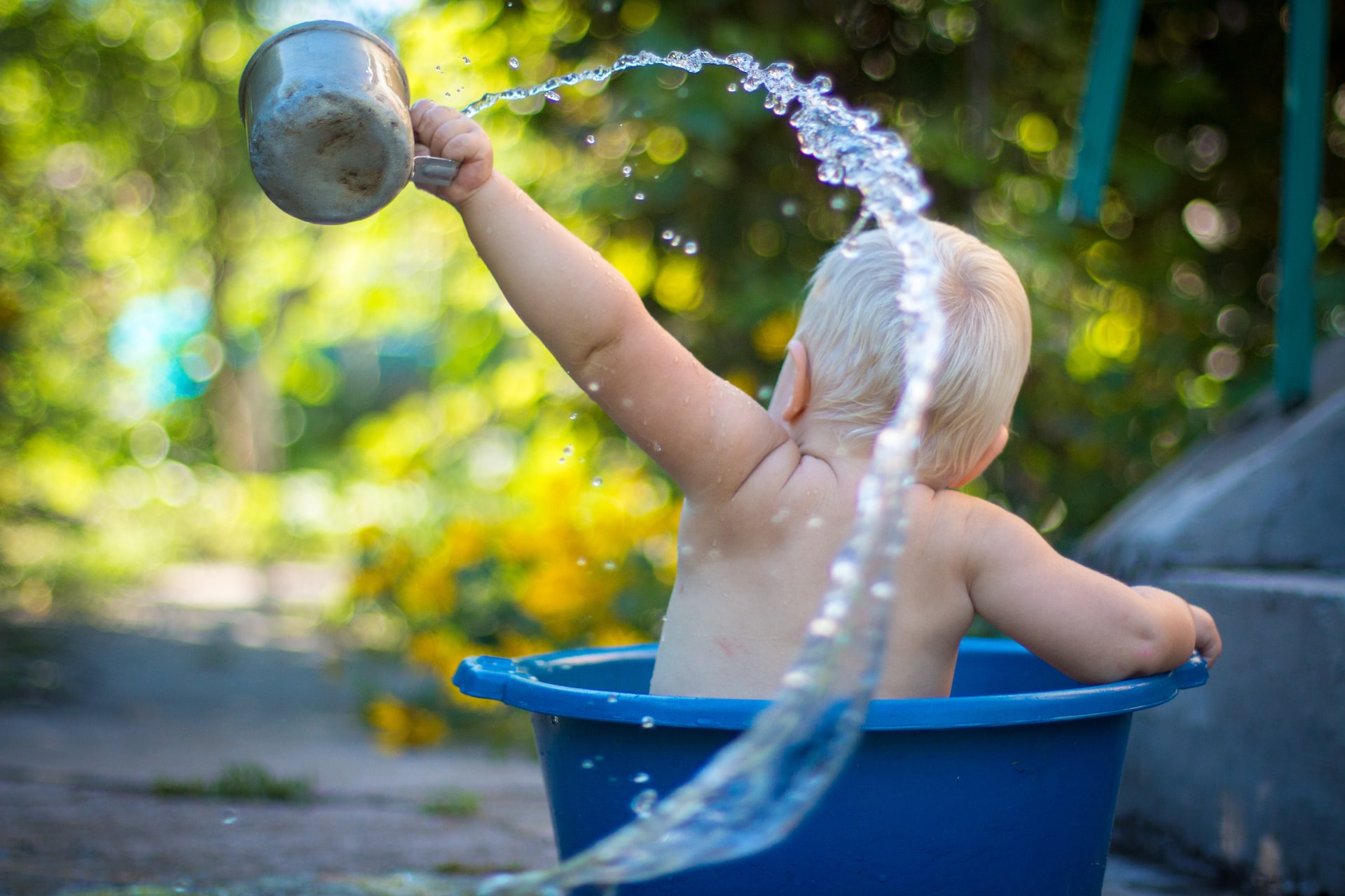 Baby holding a small jug playing with water in a bucket during summer