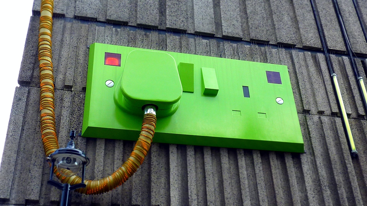 A giant green electric plug mounted on the wall of a building