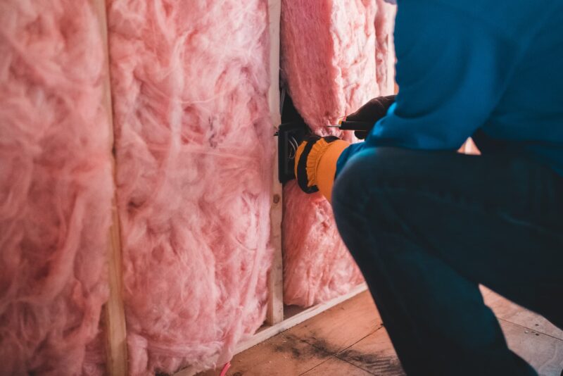Someone fitting onsulation in a wall cavity. Proper insulation is key for hitting minimum EPC standards.