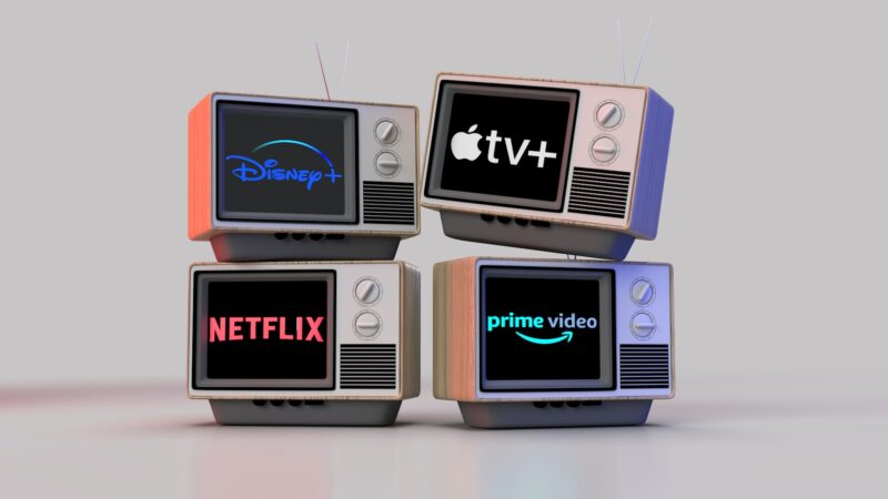 Four old-style TVs in a stack showing the logo for Netflix, Amazon Prime Video, Apple TV+ and Disney + on their screens. Tips to save on streaming all these services.