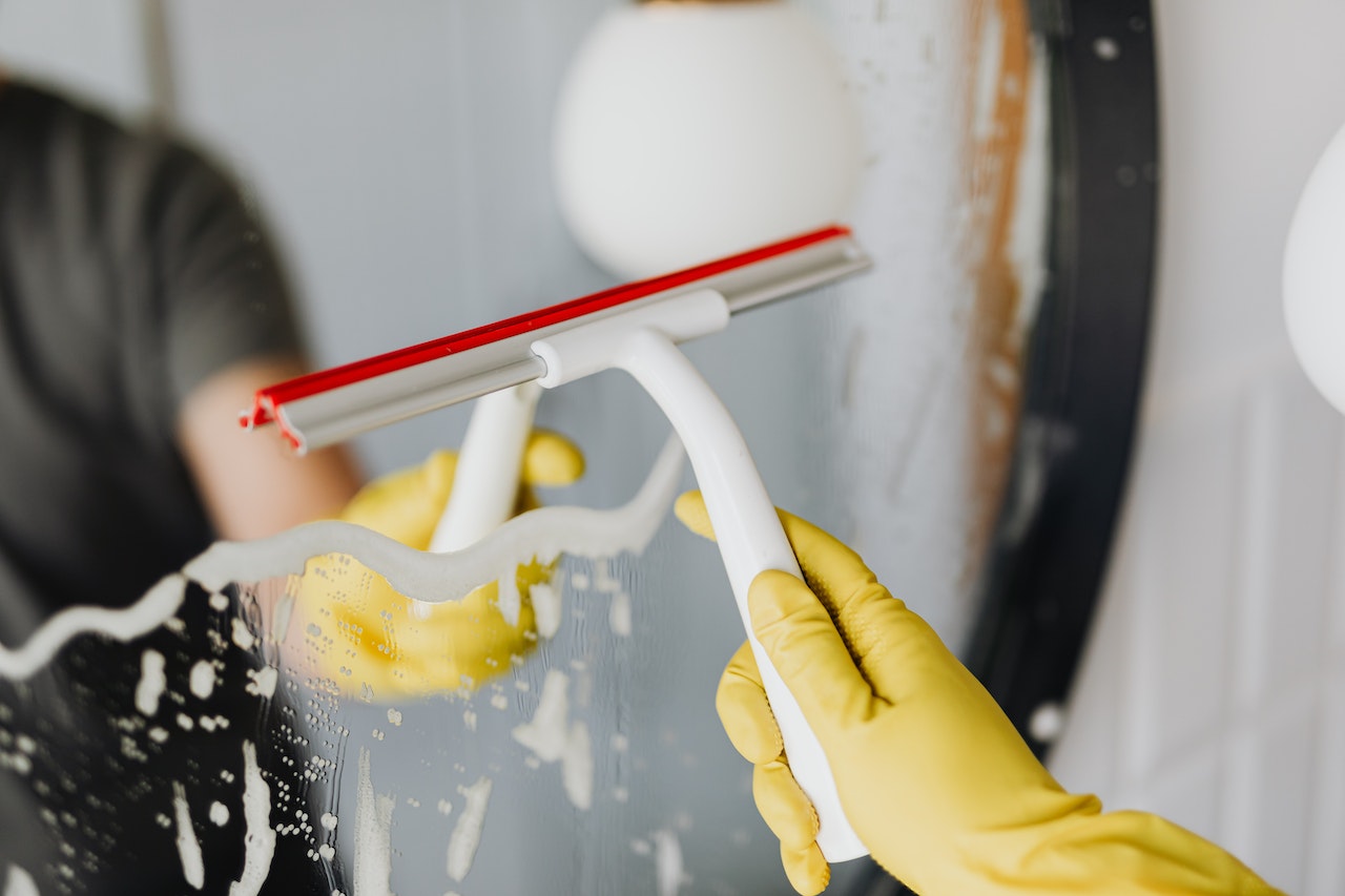 A person wearing rubber gloves cleans a mirror